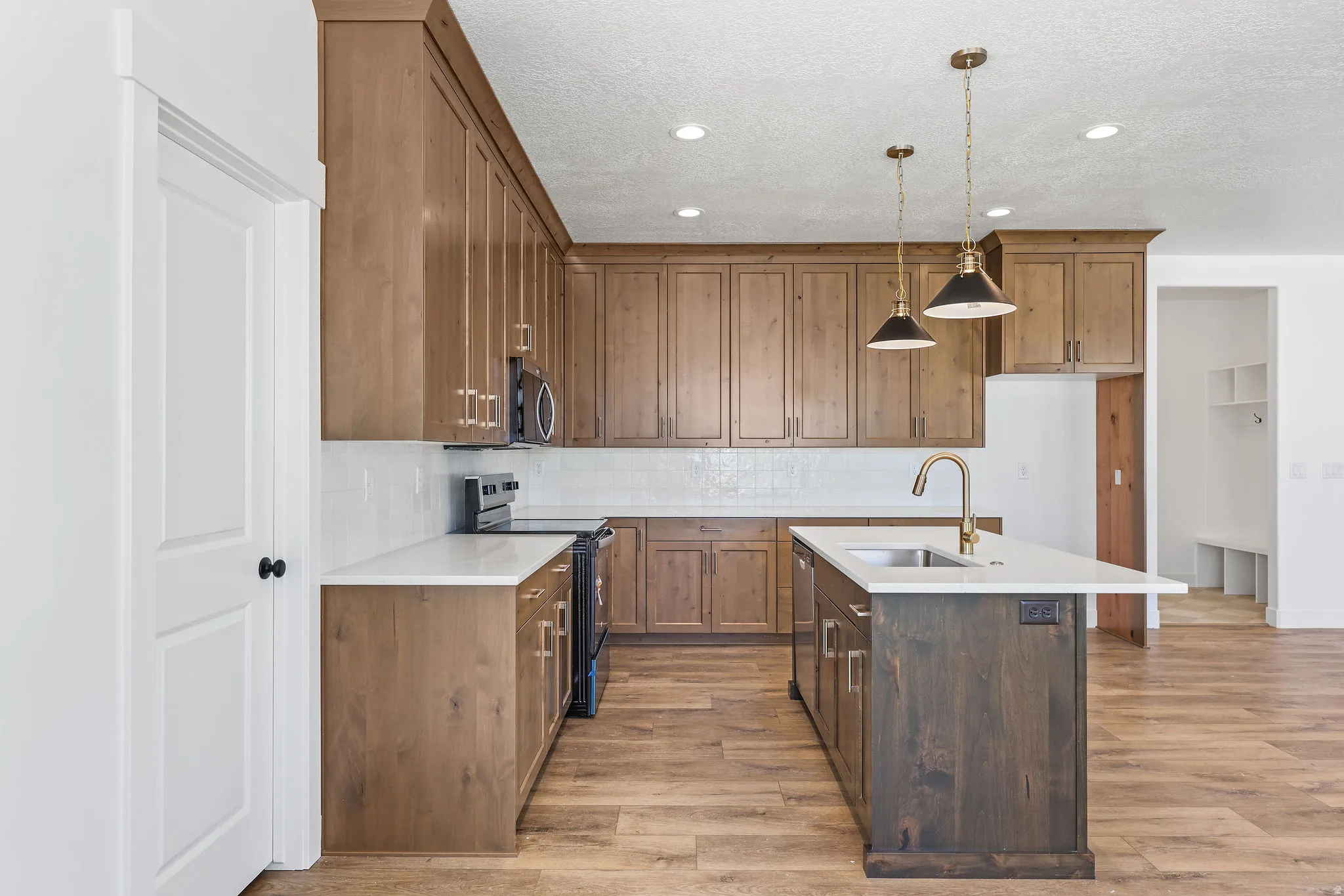 Kitchen featuring wood-finish cabinetry, white countertops, subway tile backsplash, and stainless steel sink with a brass faucet