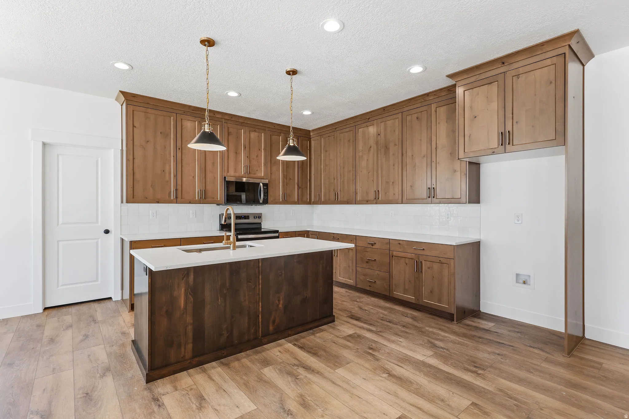 Kitchen featuring wood-finish flooring and a central island with a built-in sink and gold-tone faucet