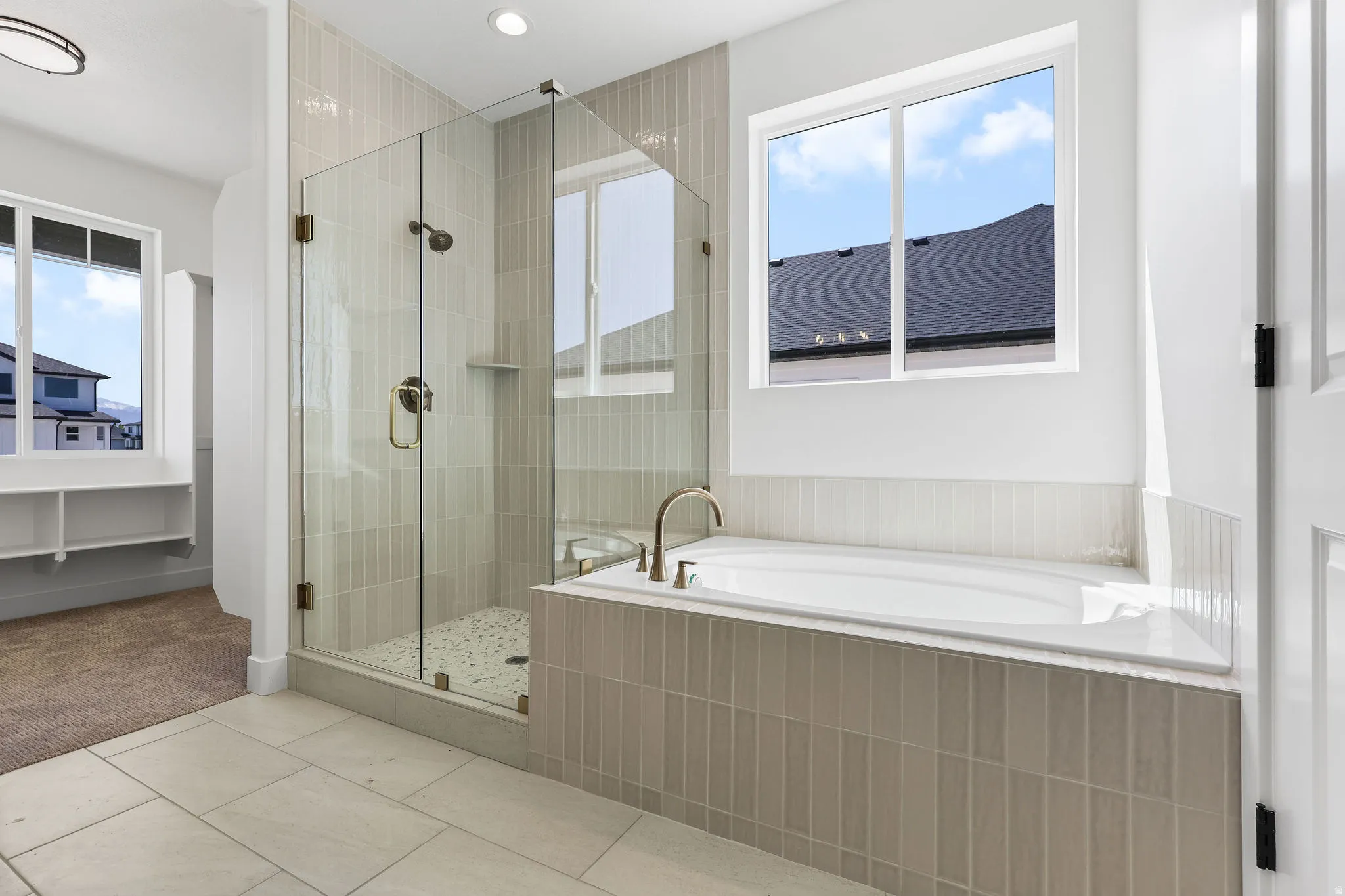 Spacious bathroom featuring a built-in soaking tub with a tiled surround, a glass-enclosed shower with vertical tile accents and pebble flooring, and light-toned floor tiling