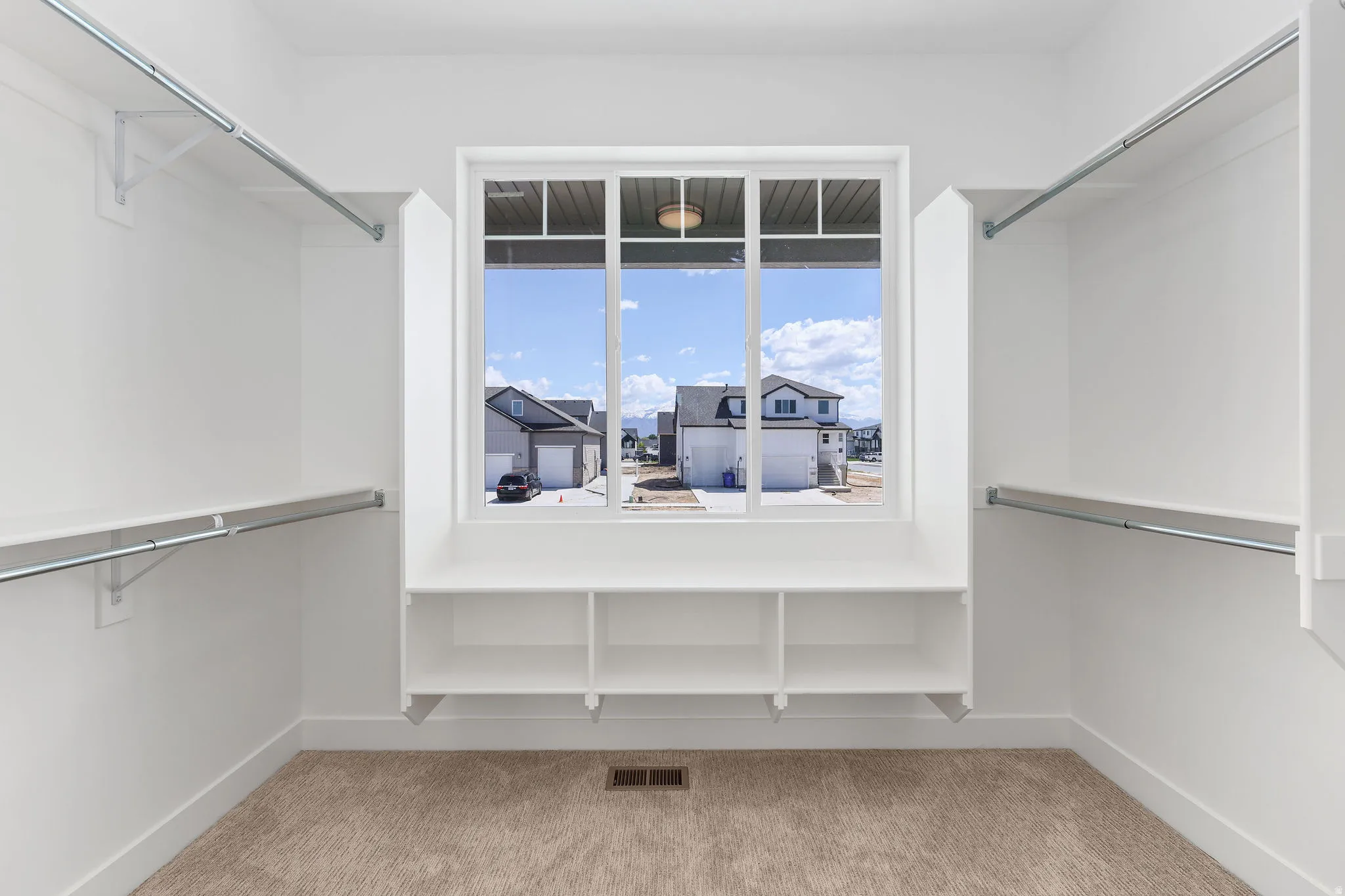 Spacious walk-in closet featuring built-in shelving, dual hanging rods, a window, and carpet flooring