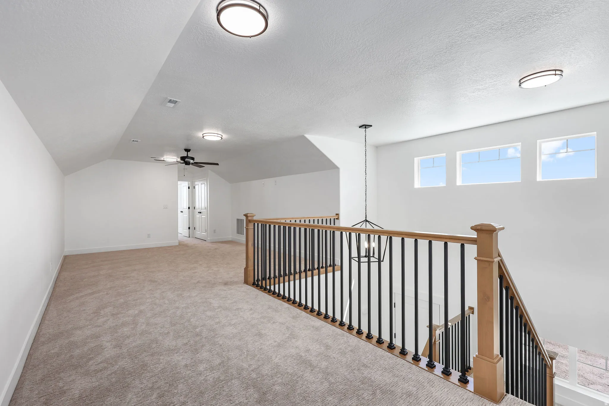 Spacious loft area featuring light-toned carpeting, a black wrought iron and natural wood banister, and three transom windows