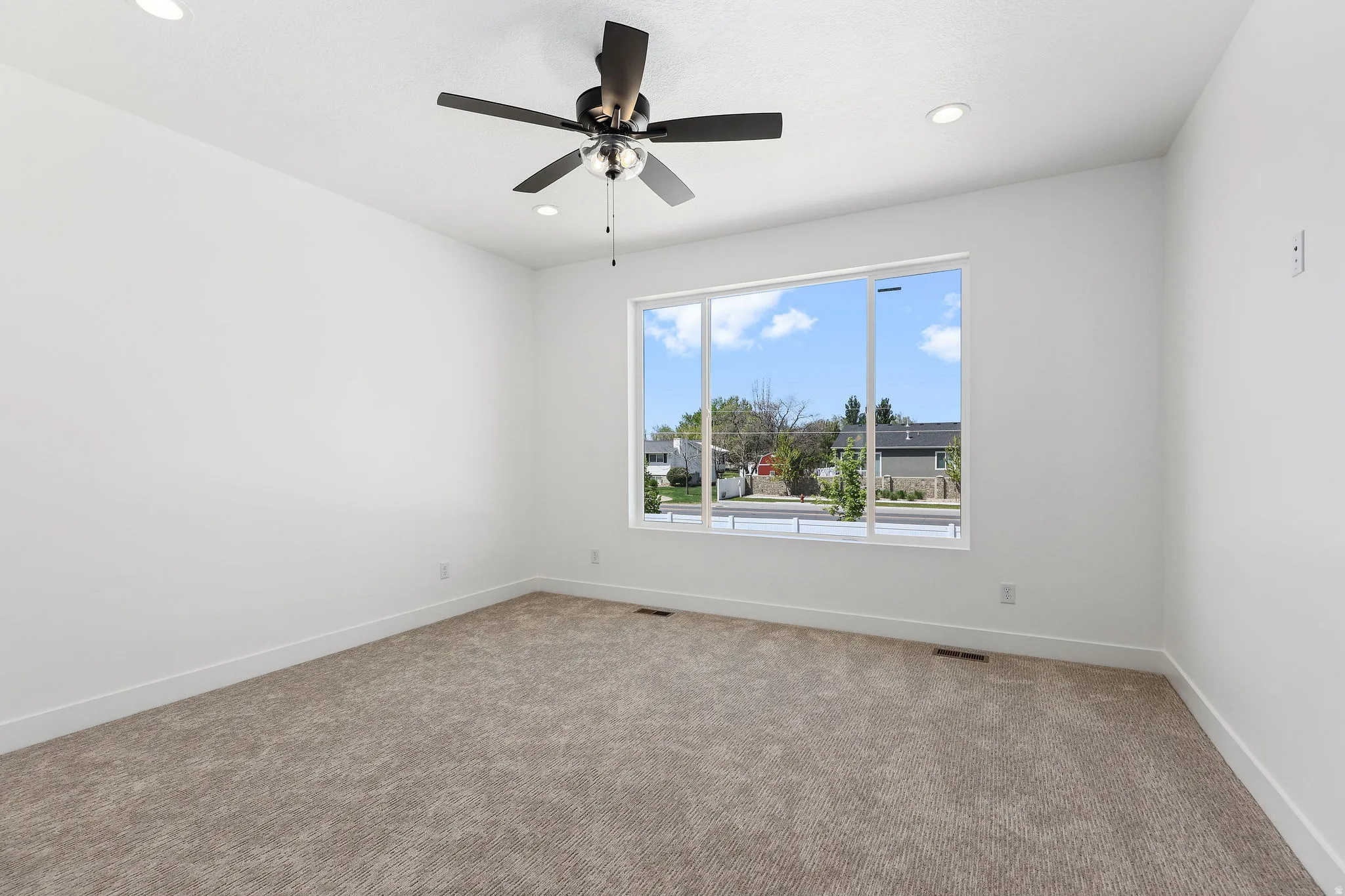 Spacious room featuring a large multi-pane window, recessed lighting, a ceiling fan with integrated lighting, neutral carpet flooring, and white baseboards