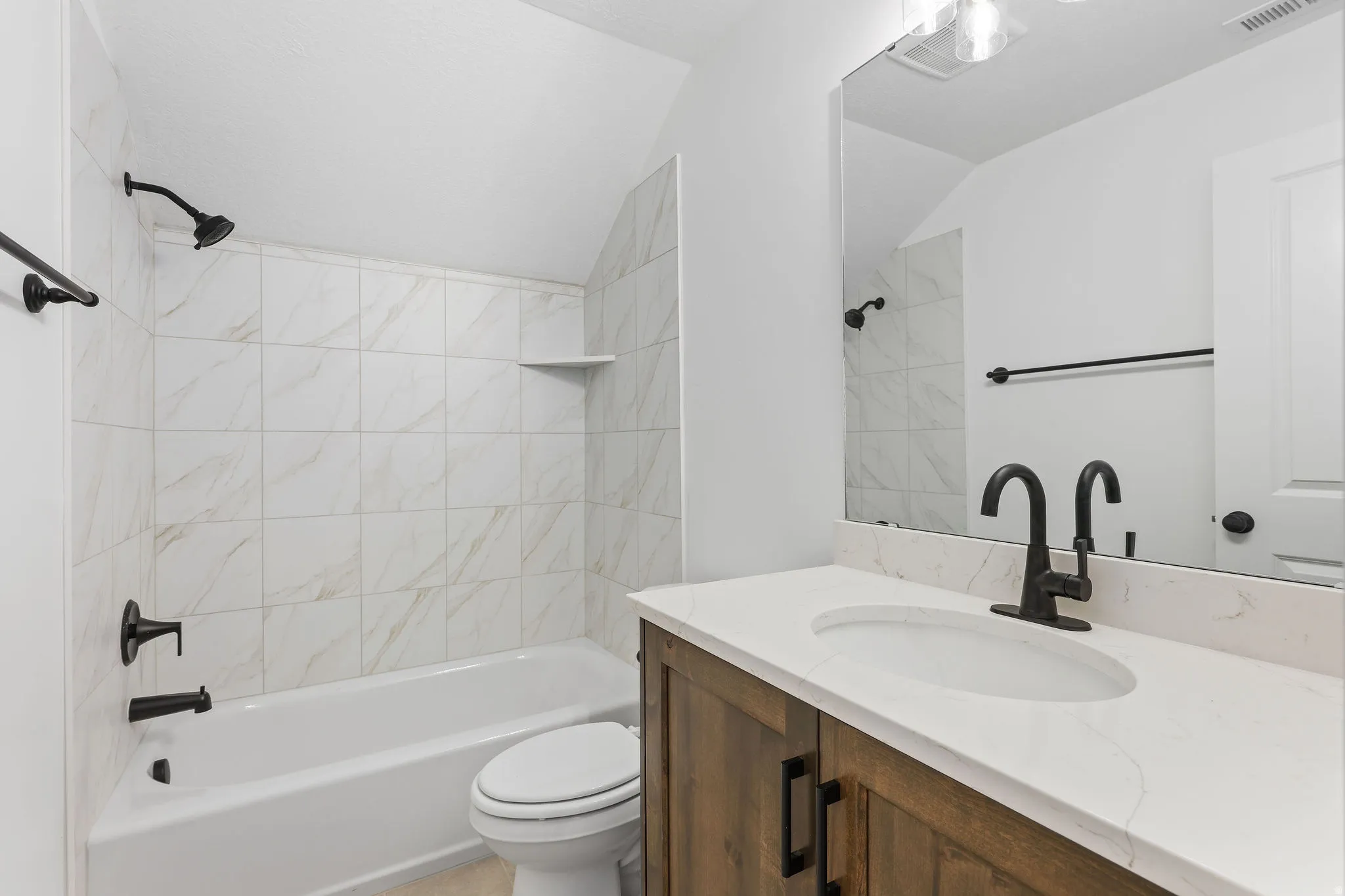 Bathroom featuring a white bathtub with a tiled surround, a wood-finish vanity with a white countertop, a single undermount sink, and matte black fixtures