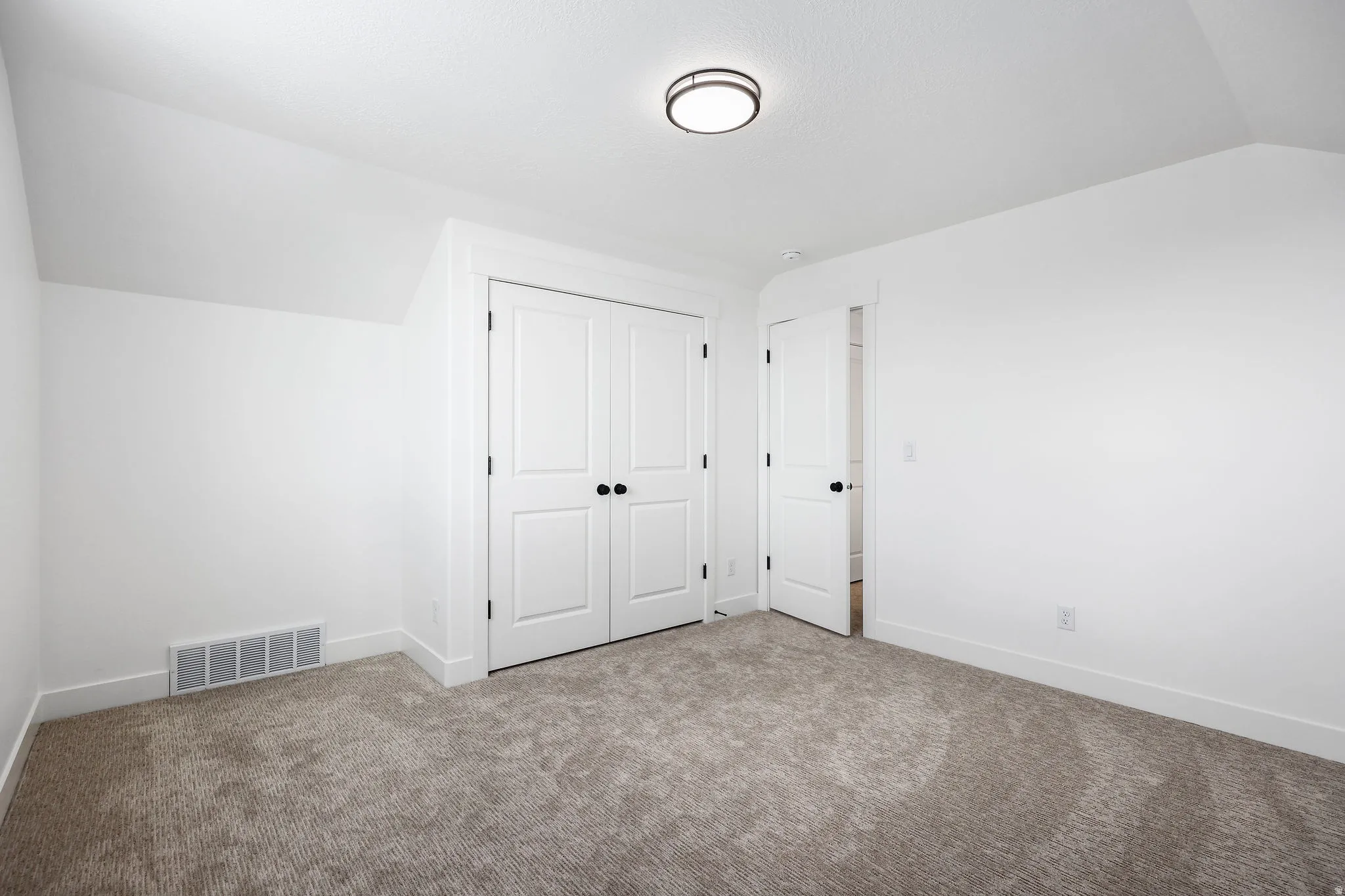 White walls and neutral carpeting define this interior space, featuring a double-door closet with black hardware