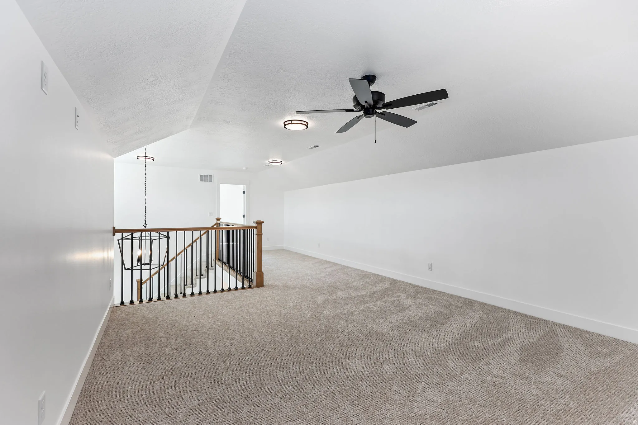 Spacious carpeted room featuring an open stairwell with black metal balusters and a dark wood handrail