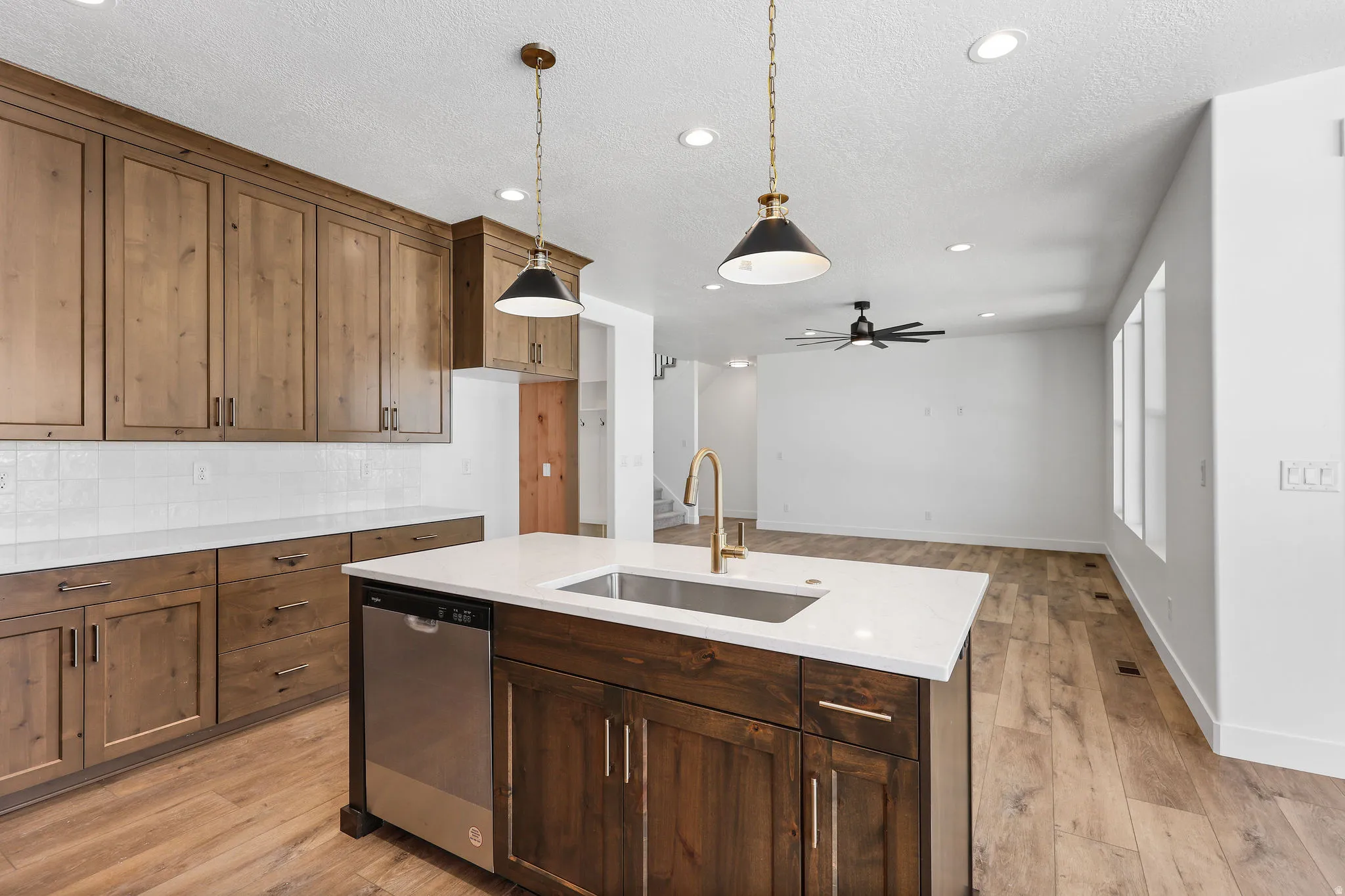 Kitchen featuring wood-finish cabinetry, a central island with a built-in sink, stainless steel dishwasher, and quartz countertops