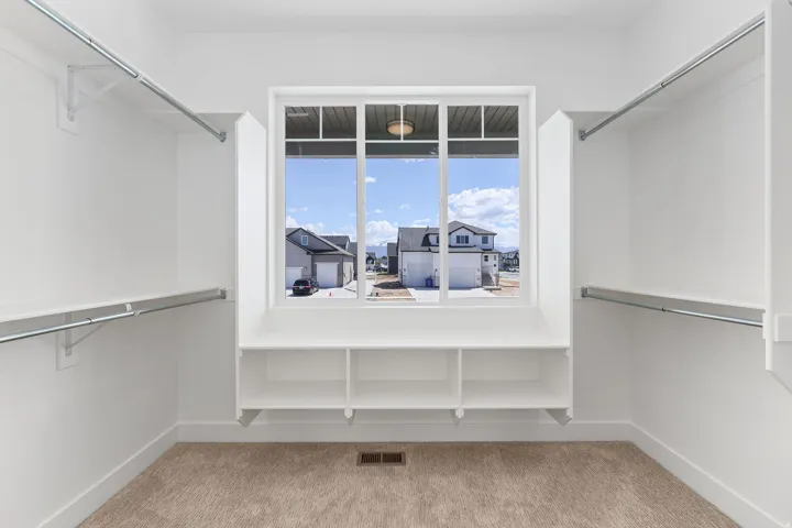 Spacious walk-in closet featuring built-in shelving, dual hanging rods, a window, and carpet flooring