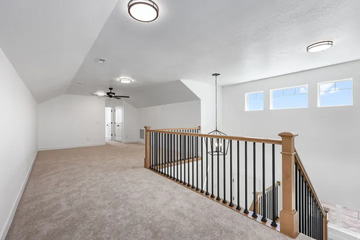 Spacious loft area featuring light-toned carpeting, a black wrought iron and natural wood banister, and three transom windows