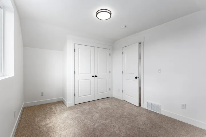 Bedroom featuring plush carpet flooring, white painted walls, a built-in closet with bifold doors, and a window for natural light