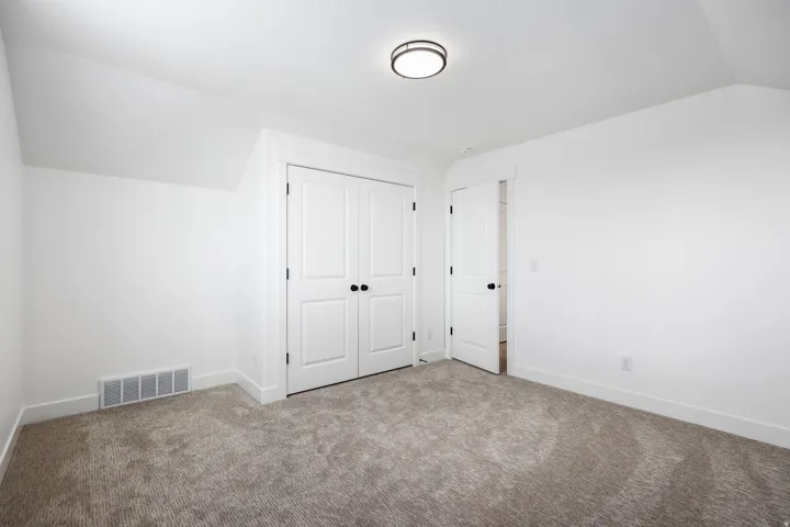 White walls and neutral carpeting define this interior space, featuring a double-door closet with black hardware
