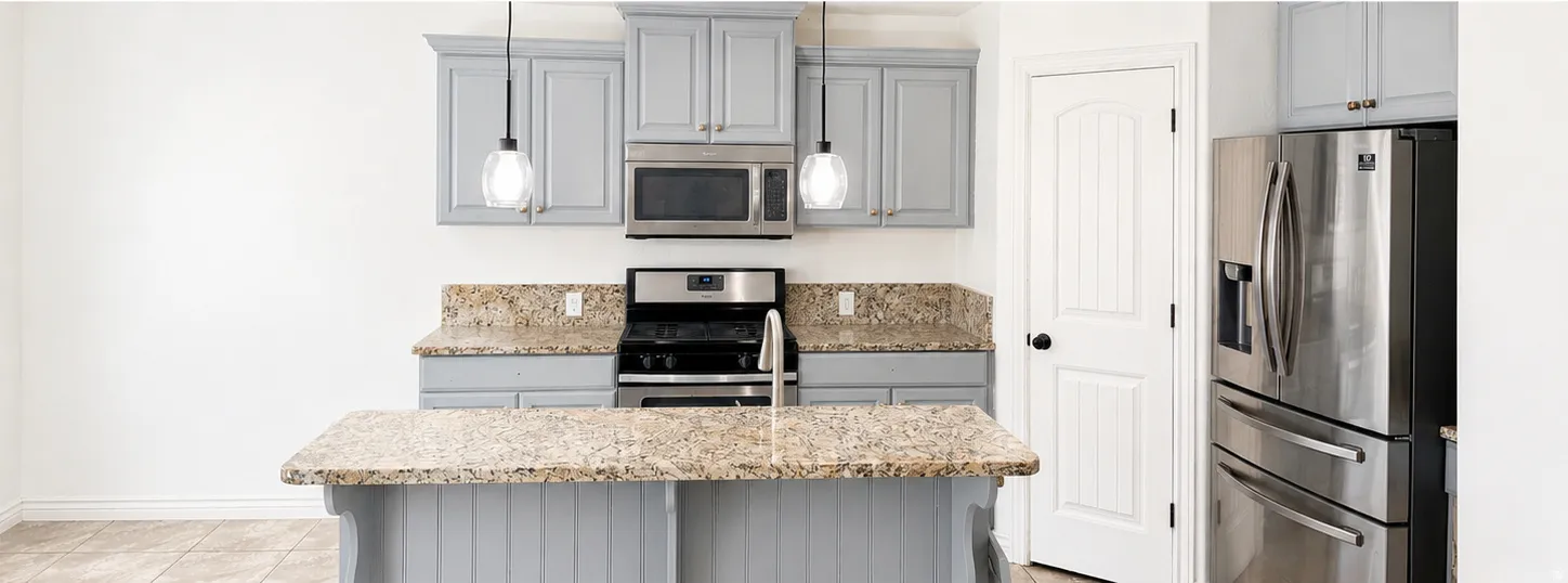 Modern kitchen featuring light gray cabinetry, granite countertops, stainless steel appliances, and an eat-at island with pendant lighting