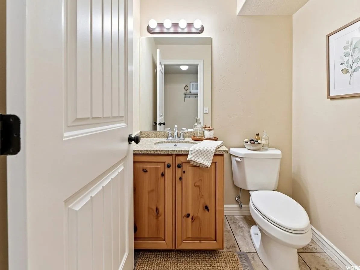 Well-appointed bathroom featuring a white panel door, a wood-finish vanity with a light-toned countertop, a rectangular mirror, and a white toilet