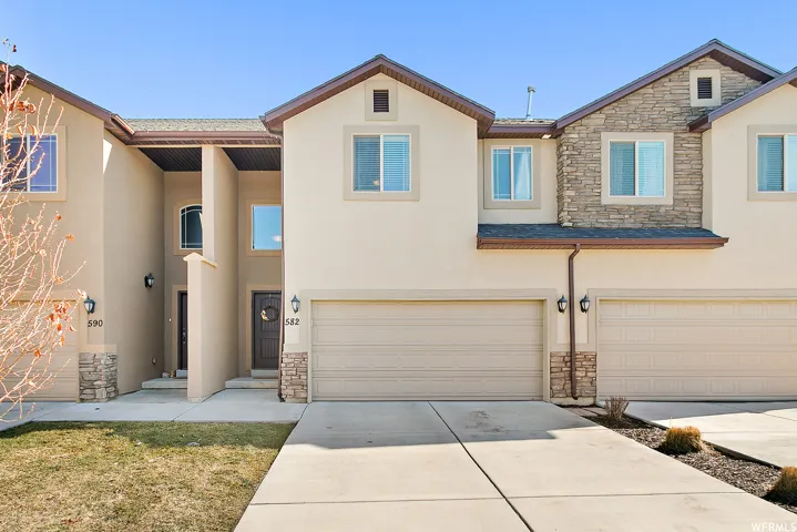 Traditional-style home featuring stone siding, stucco siding, a garage, and driveway