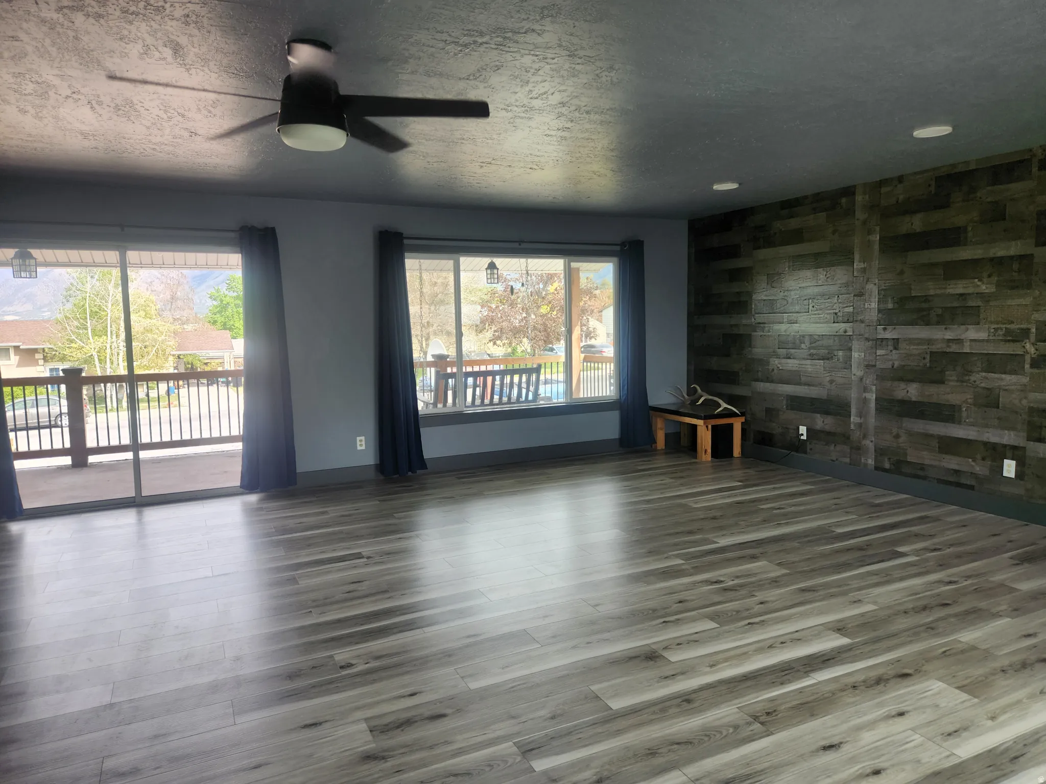 Spare room featuring a ceiling fan, a textured ceiling, wood walls, wood finished floors, and an accent wall
