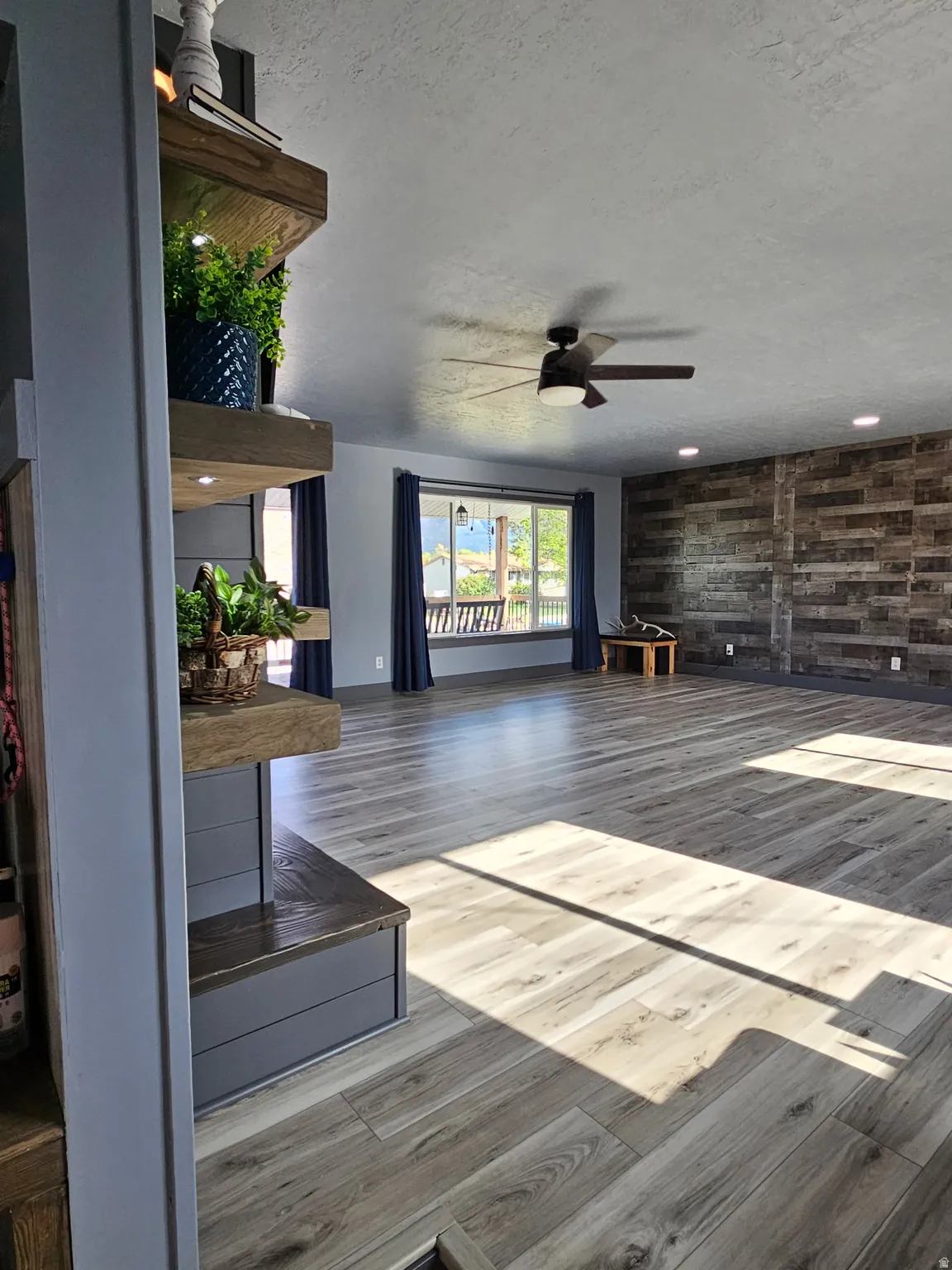 Unfurnished living room with a textured ceiling, ceiling fan, wood finished floors, and wood walls