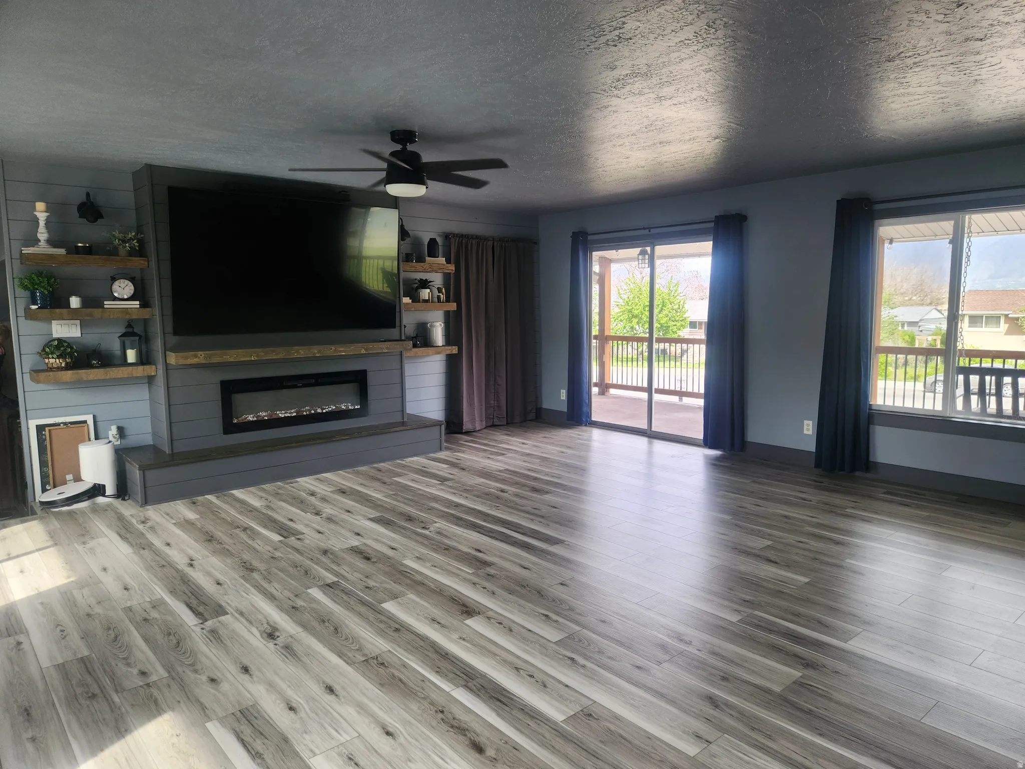 Unfurnished living room featuring a ceiling fan, a textured ceiling, a glass covered fireplace, and dark wood finished floors