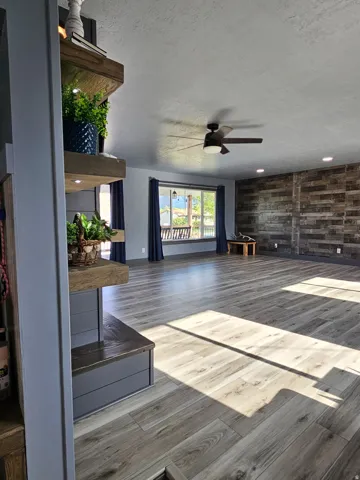 Unfurnished living room with a textured ceiling, ceiling fan, wood finished floors, and wood walls