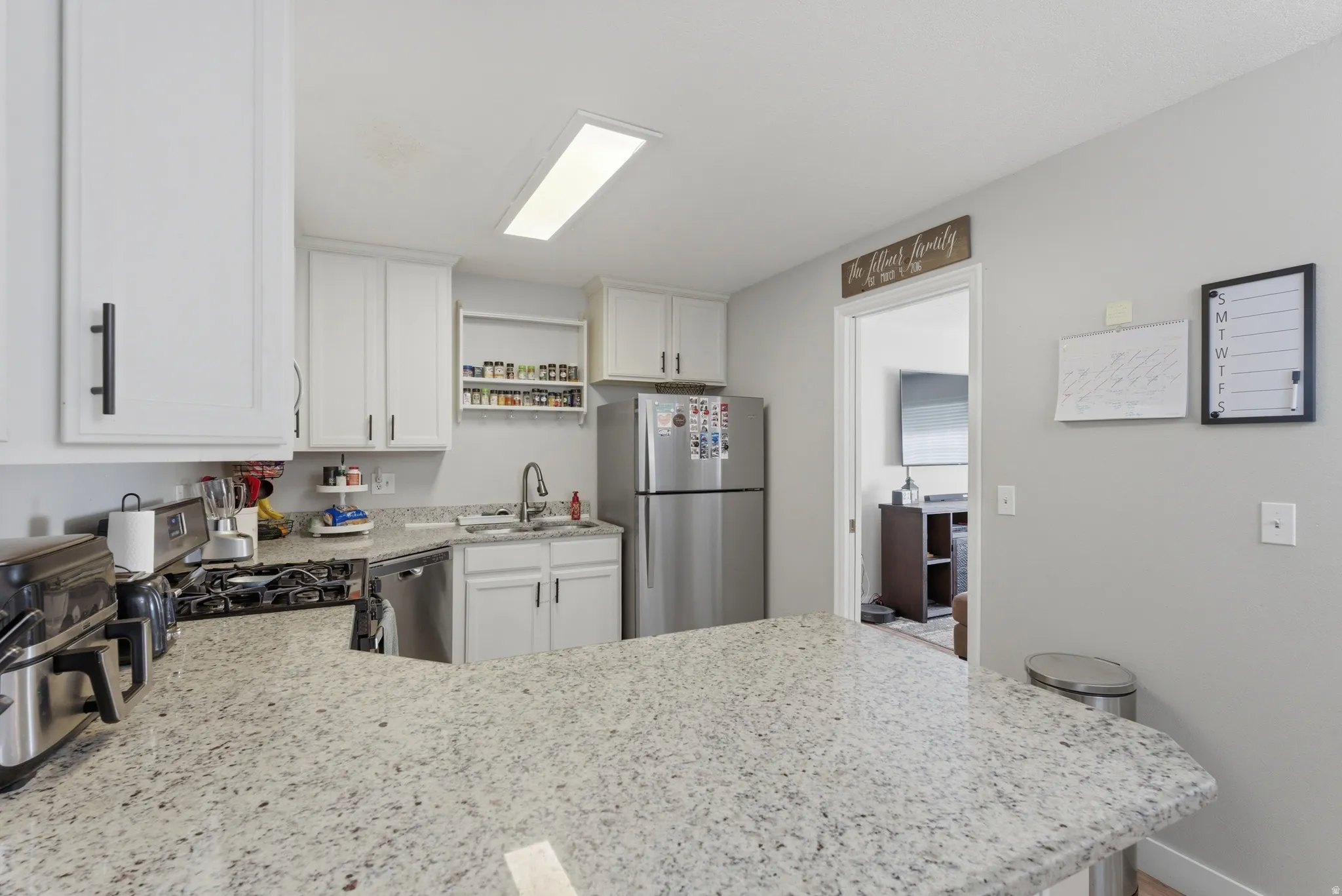 Kitchen with stainless steel appliances, a peninsula, white cabinetry, and light stone counters