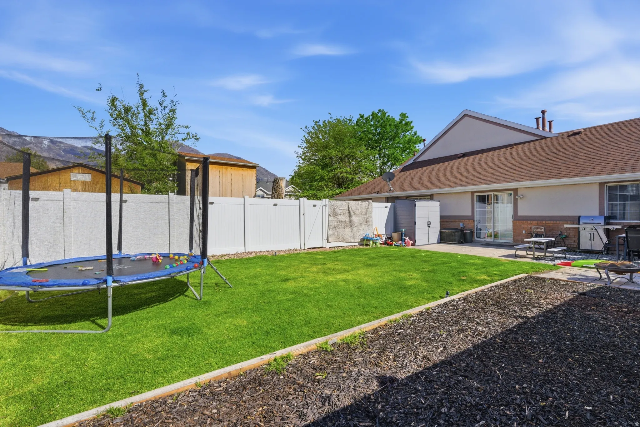 Fenced backyard with a trampoline, a patio area, and a gate