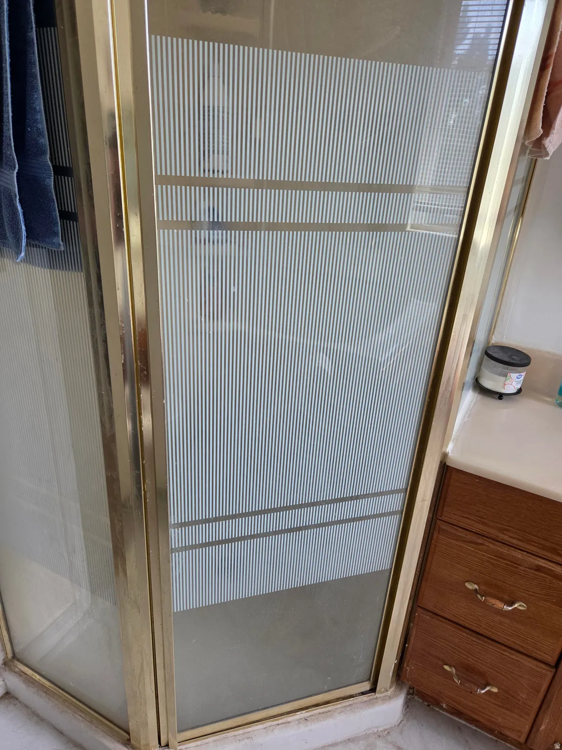 Shower enclosure with patterned glass, gold-tone frame, and adjacent vanity with wood-finish cabinetry