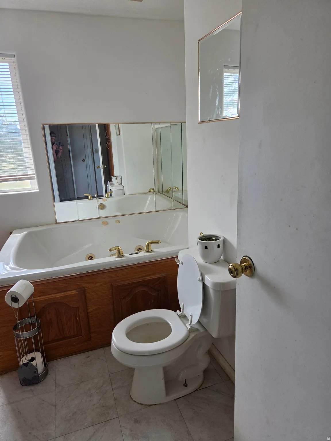 Built-in jetted tub with wood-finish paneling, white toilet, and window with blinds