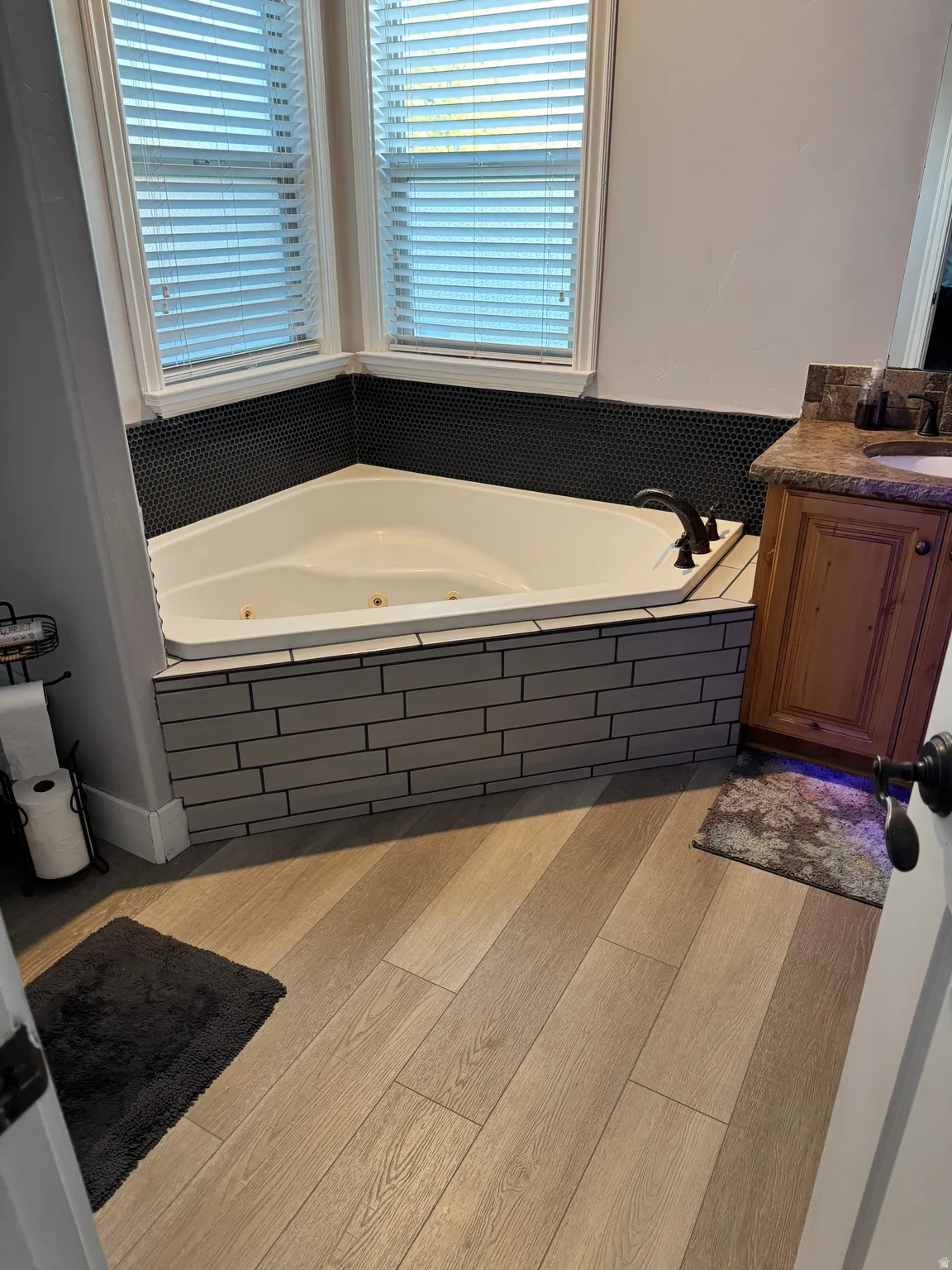 Corner jetted tub with dark penny tile backsplash and grey subway tile surround