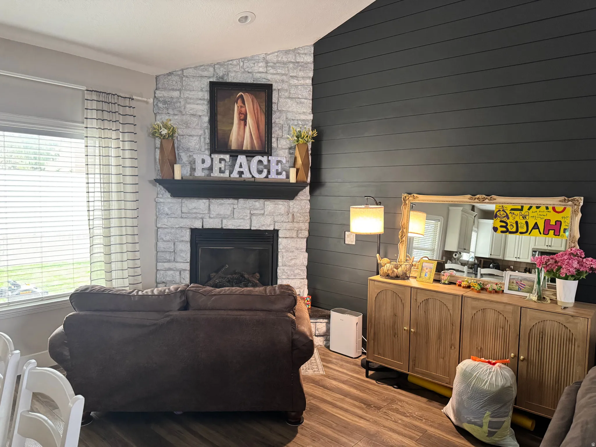 Living area featuring dark wood-type flooring, vaulted ceiling, a stone fireplace, and wood walls