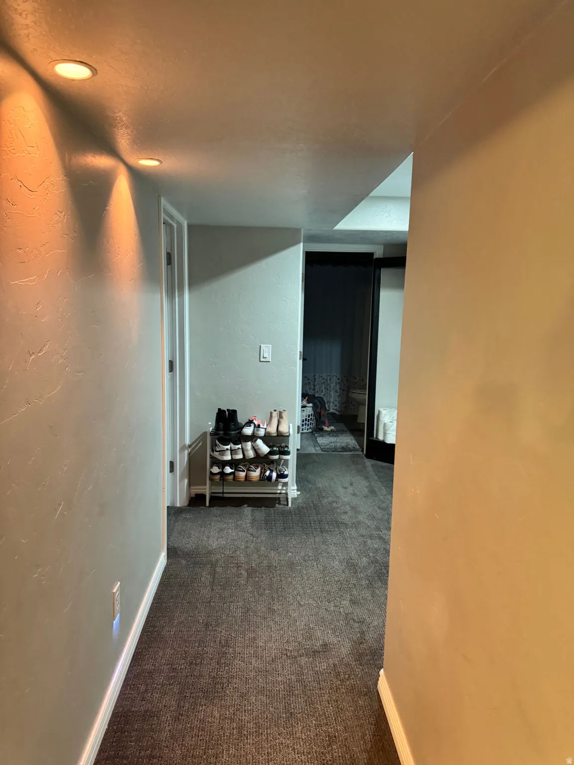 Corridor featuring dark colored carpet and a textured wall