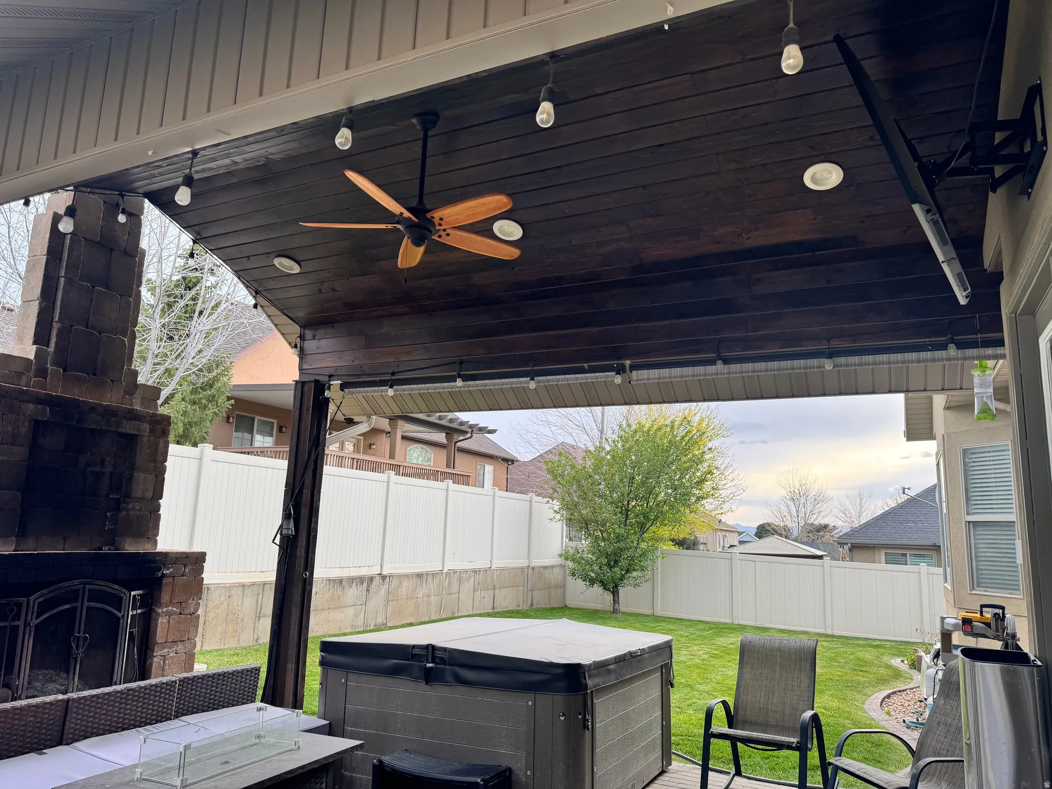 Fenced backyard featuring a ceiling fan, an outdoor stone fireplace, and a hot tub