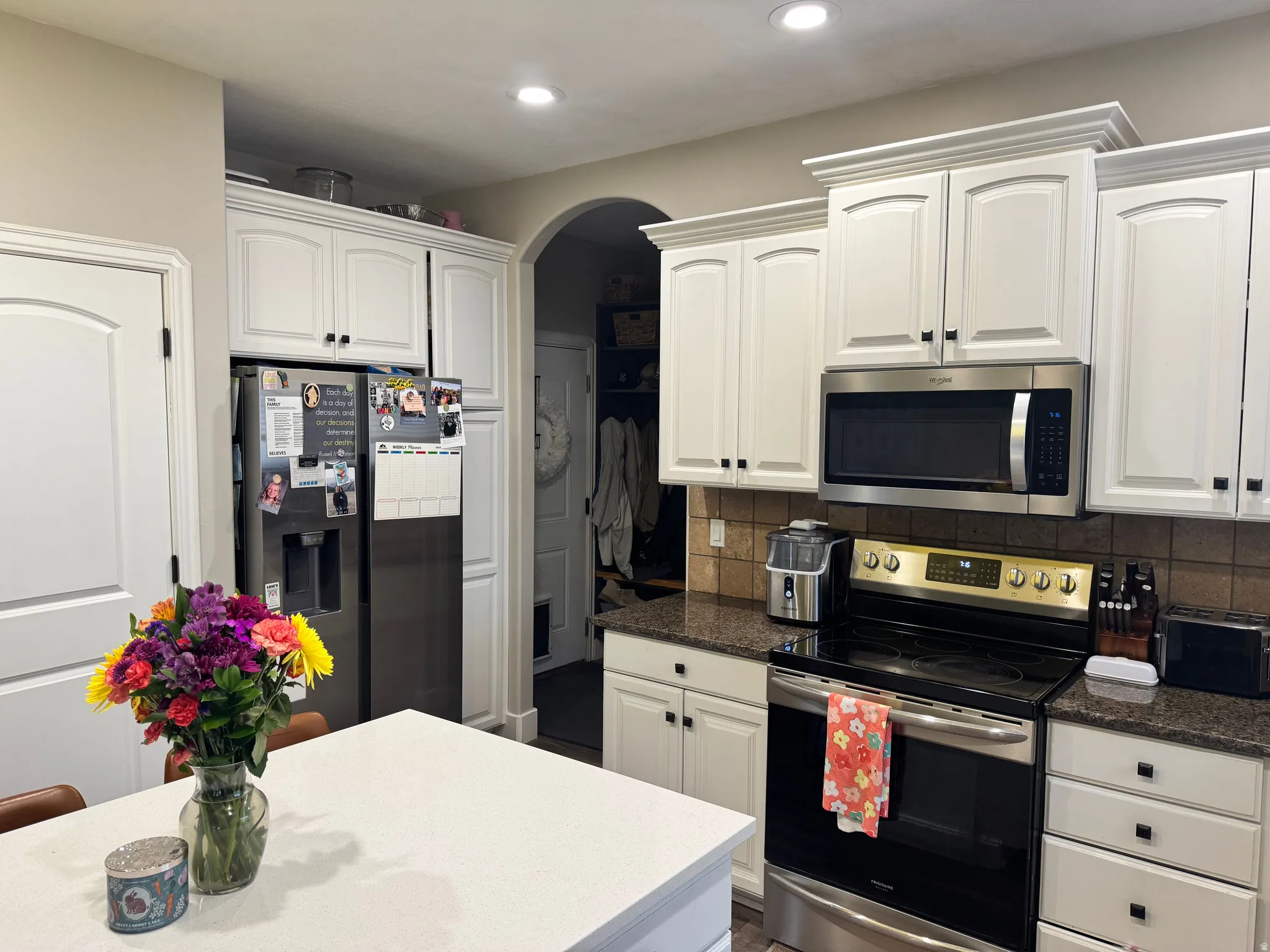 Kitchen featuring stainless steel appliances, white cabinets, backsplash, arched walkways, and dark stone counters