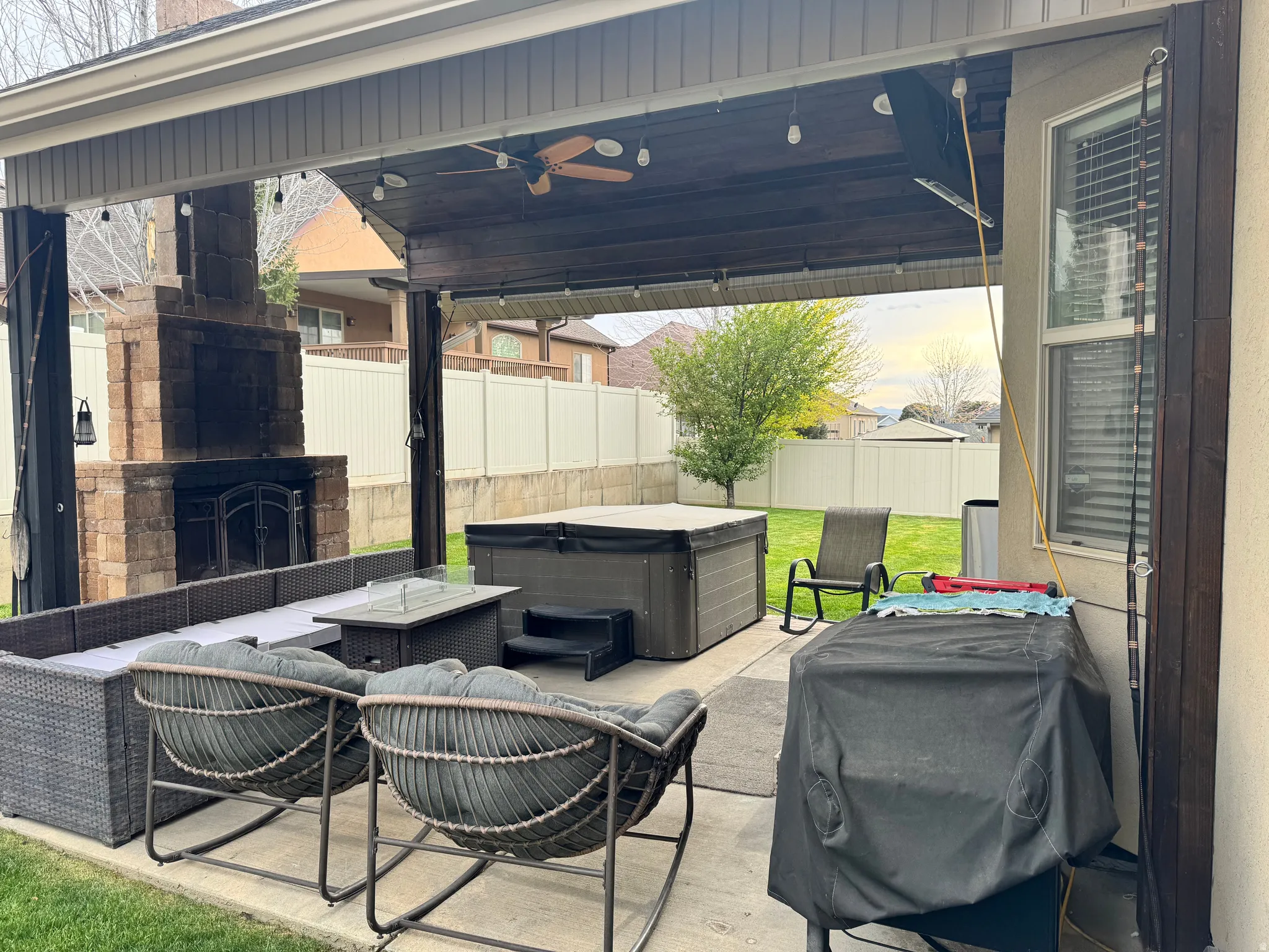 Fenced backyard featuring a patio area, an outdoor living space with a fireplace, a grill, ceiling fan, and a hot tub