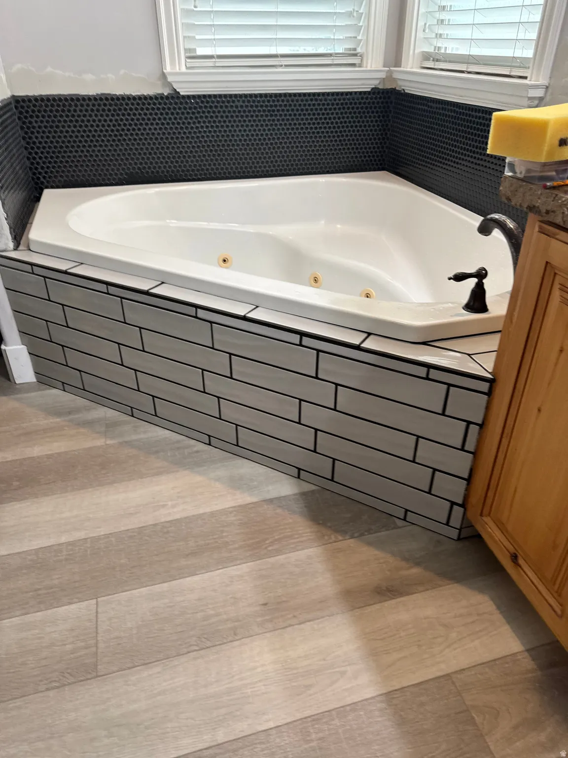 Corner jetted tub featuring a dark bronze faucet, surrounded by light gray subway tile