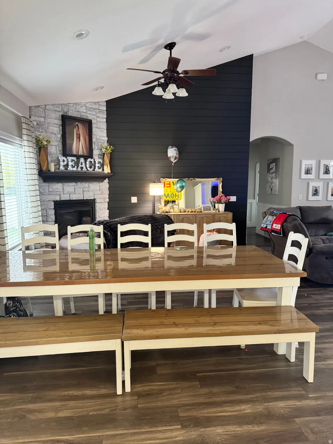 Dining room featuring arched walkways, ceiling fan, dark wood-type flooring, a fireplace, and wood walls