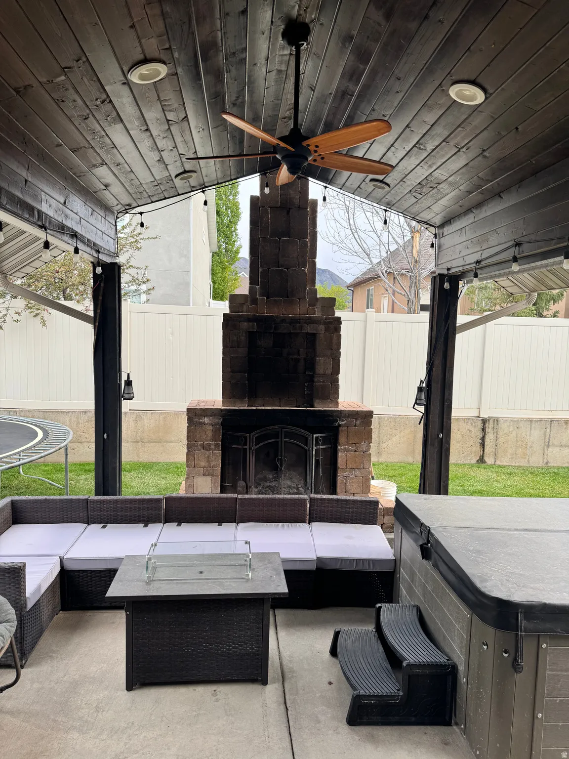 Fenced backyard featuring an outdoor living space with a fireplace, a patio, a ceiling fan, and a trampoline