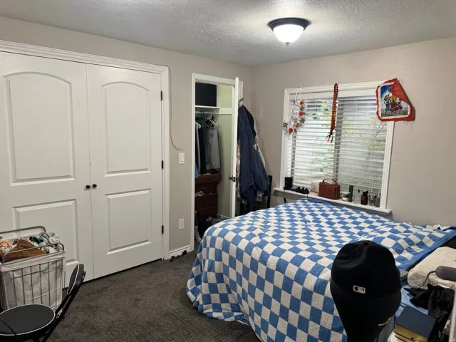 Bedroom with a closet, dark carpet, and a textured ceiling