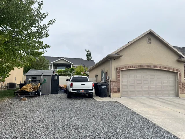 View of front of property featuring driveway, brick siding, stucco siding, and an attached garage