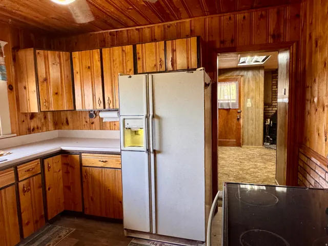 Kitchen featuring wood walls, wood finish cabinets, white refrigerator with ice dispenser, and light countertops