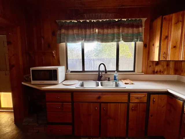 Kitchen with wood finish cabinetry, wood walls, light countertops, and white microwave
