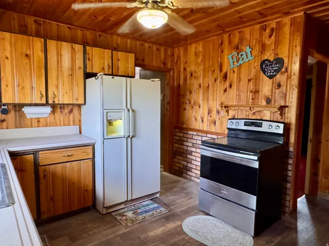 Kitchen with white refrigerator with ice dispenser, stainless steel electric range, wood finish cabinets, light countertops, and dark wood-style flooring