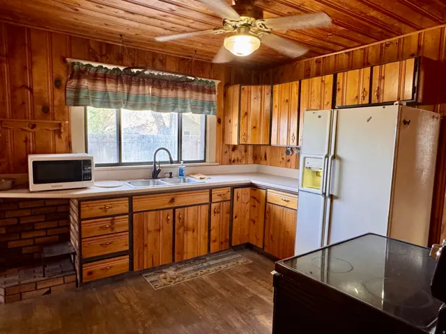 Kitchen with white refrigerator with ice dispenser, black electric range, wood finish cabinetry, light countertops, and a ceiling fan