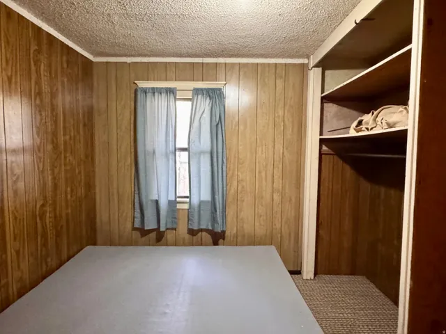 Bedroom featuring a textured ceiling and wood walls
