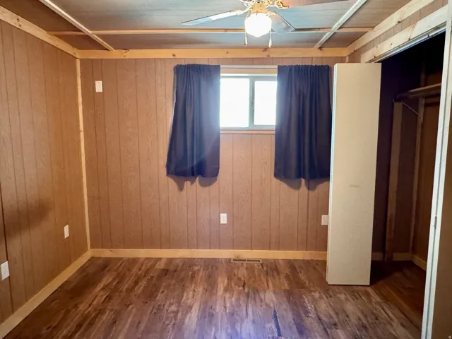 Unfurnished bedroom with dark wood-style floors, ceiling fan, wooden walls, and a closet