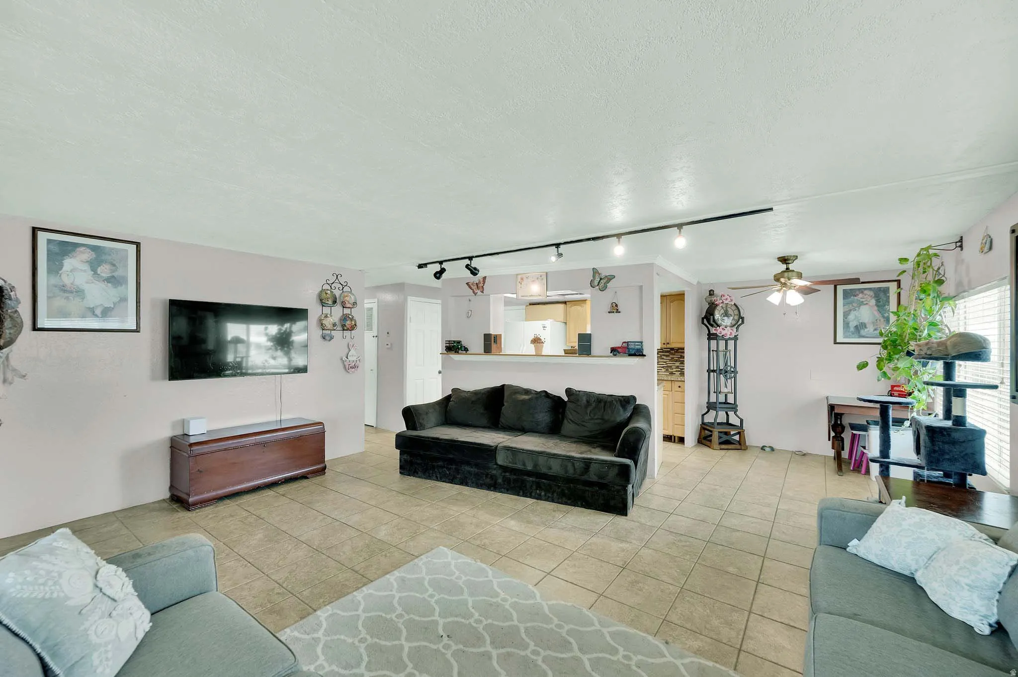 Living room featuring a textured ceiling, rail lighting, light tile patterned flooring, and a ceiling fan