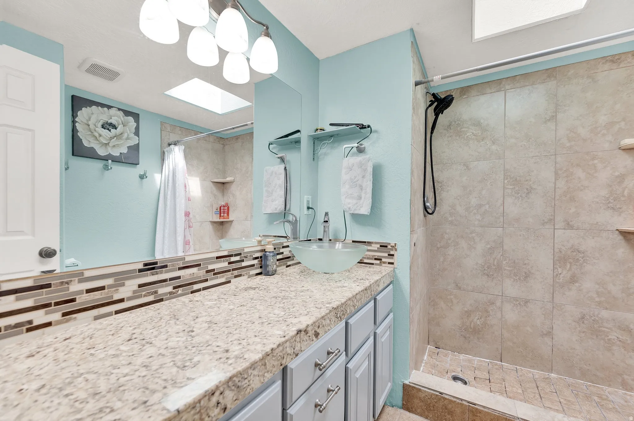 Full bathroom with vanity, a tile shower, a skylight, and backsplash