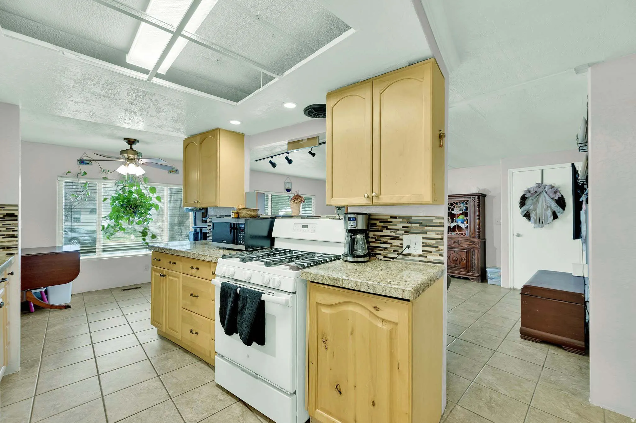 Kitchen with light wood finish cabinetry, white gas stove, decorative backsplash, light tile patterned floors, and recessed lighting