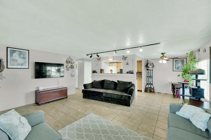 Living room featuring a textured ceiling, rail lighting, light tile patterned flooring, and a ceiling fan