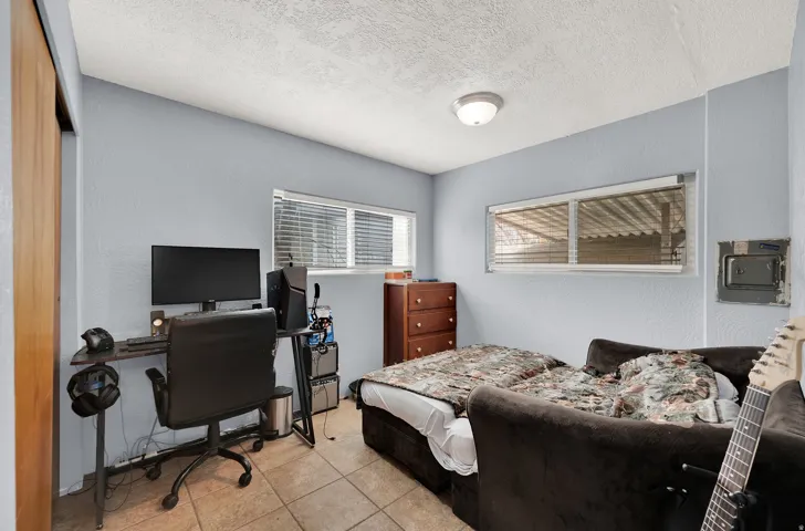Bedroom featuring an office area, a textured wall, a textured ceiling, and light tile patterned floors