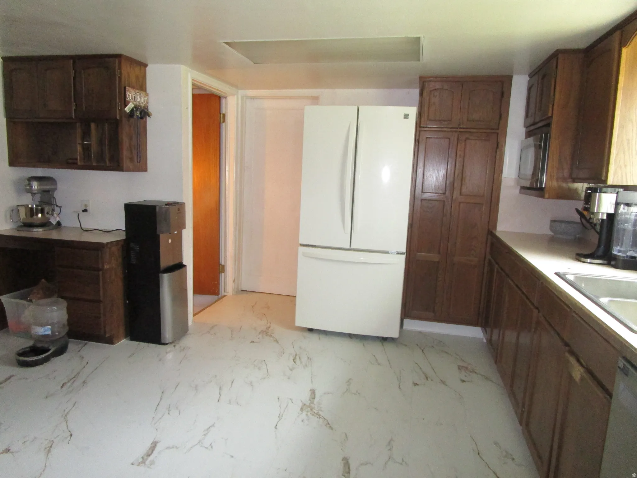Kitchen featuring freestanding refrigerator, dishwashing machine, light marble finish floors, and light countertops