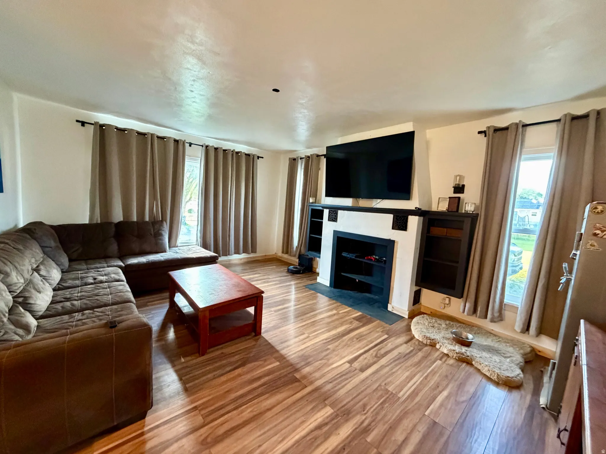 Living area with wood-finish flooring, a fireplace featuring a black mantel, and integrated shelving