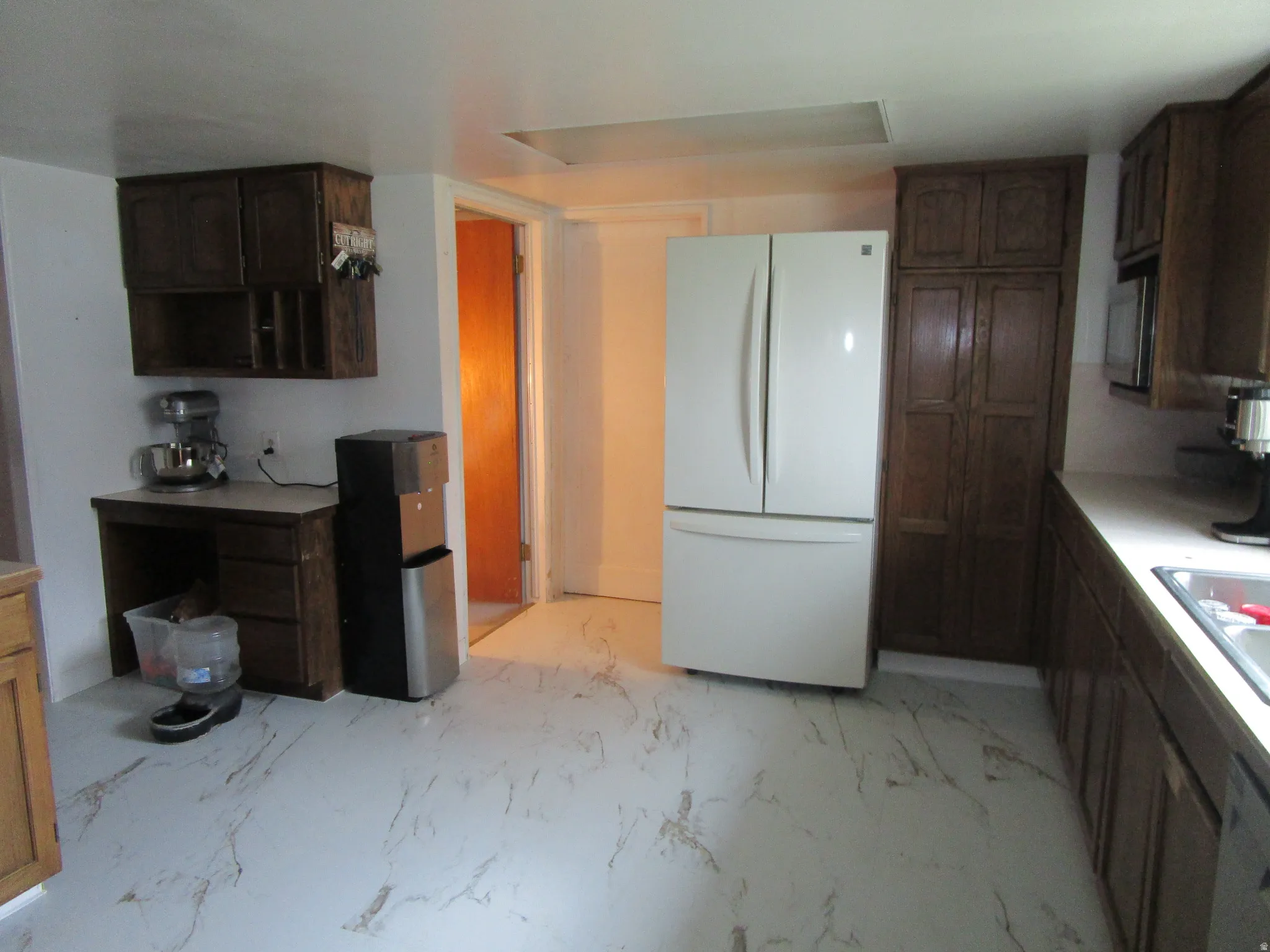 Kitchen with freestanding refrigerator, dark wood finish cabinetry, light countertops, light marble finish flooring, and stainless steel dishwasher